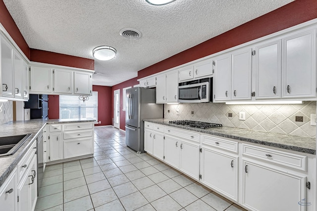 kitchen with light tile patterned floors, stainless steel appliances, tasteful backsplash, a textured ceiling, and white cabinets