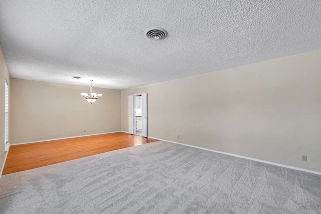 unfurnished room with carpet flooring, a textured ceiling, and an inviting chandelier