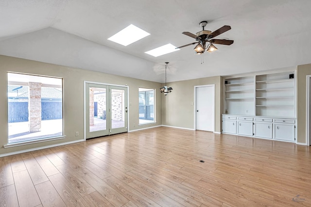 unfurnished living room featuring ceiling fan with notable chandelier, lofted ceiling with skylight, and light hardwood / wood-style floors