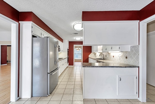 kitchen with sink, light tile patterned floors, stainless steel fridge, white cabinets, and backsplash