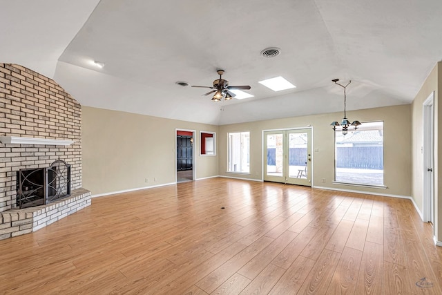 unfurnished living room with vaulted ceiling, a brick fireplace, ceiling fan with notable chandelier, and light wood-type flooring