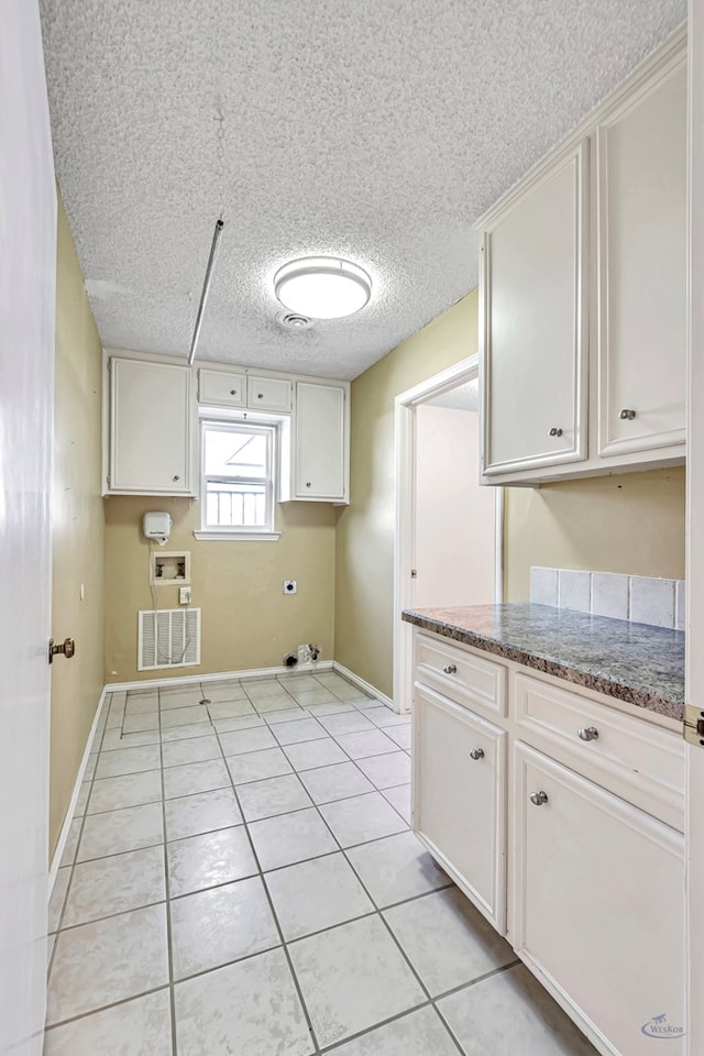 washroom with light tile patterned flooring, cabinets, a textured ceiling, hookup for a washing machine, and hookup for an electric dryer