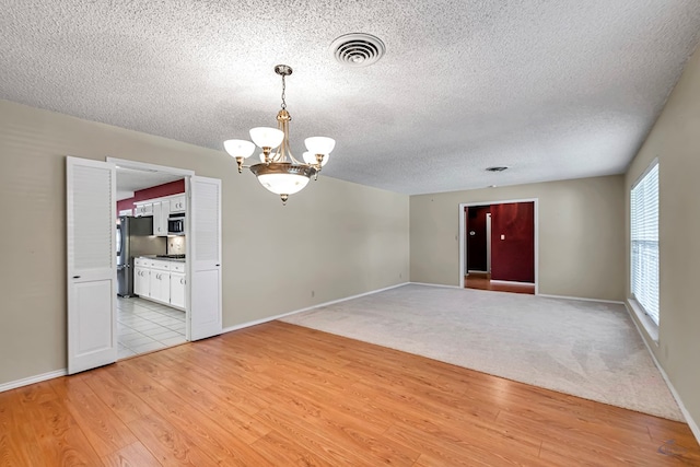 unfurnished room with an inviting chandelier, a textured ceiling, and light wood-type flooring