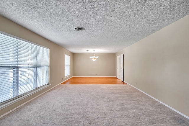 unfurnished room featuring a textured ceiling, light colored carpet, and a chandelier