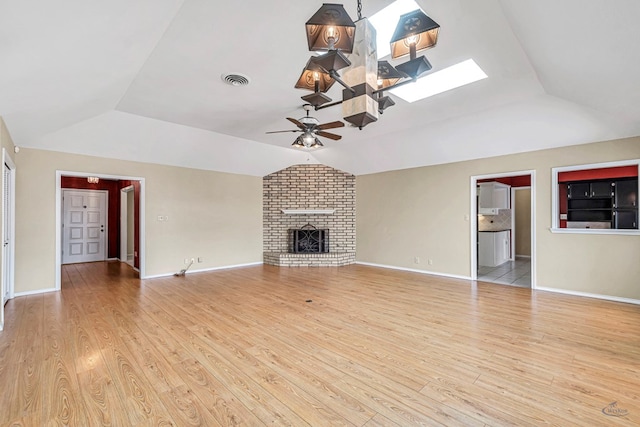 unfurnished living room with ceiling fan, a fireplace, vaulted ceiling with skylight, and light hardwood / wood-style flooring