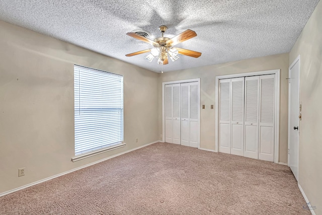 unfurnished bedroom with ceiling fan, carpet flooring, two closets, and a textured ceiling