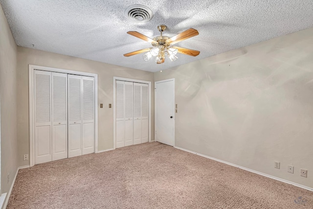 unfurnished bedroom featuring multiple closets, ceiling fan, carpet, and a textured ceiling