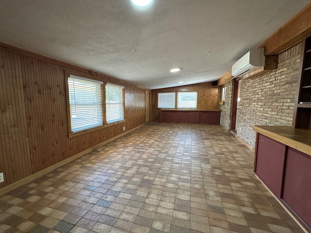 interior space featuring wood walls, baseboards, a textured ceiling, and a wall mounted air conditioner