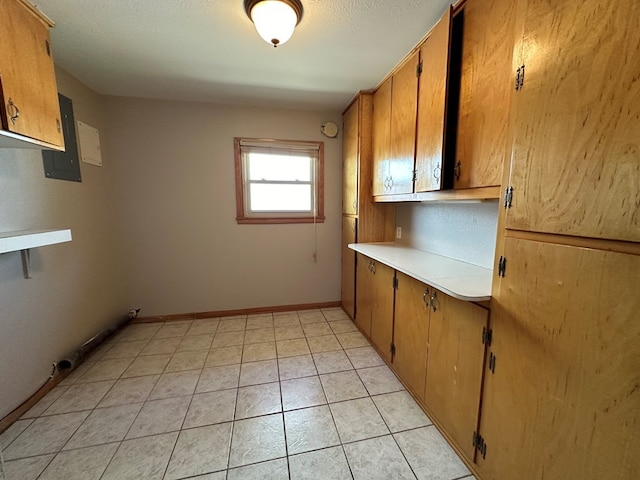 kitchen featuring light countertops, brown cabinetry, light tile patterned flooring, electric panel, and baseboards