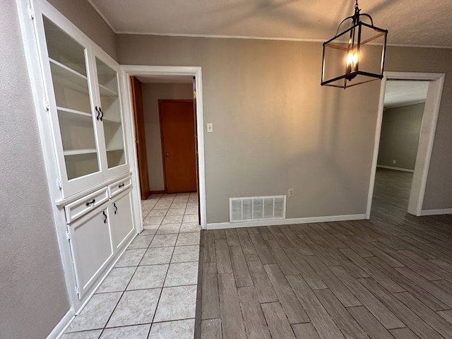 unfurnished dining area featuring built in shelves, visible vents, light wood-style flooring, ornamental molding, and baseboards