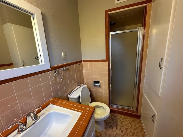 bathroom with tile walls, a sink, a shower stall, and toilet