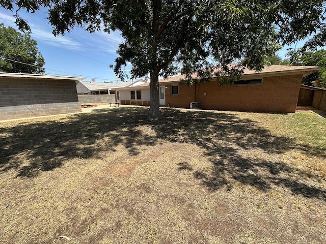 rear view of house with a yard, brick siding, fence, and central AC unit