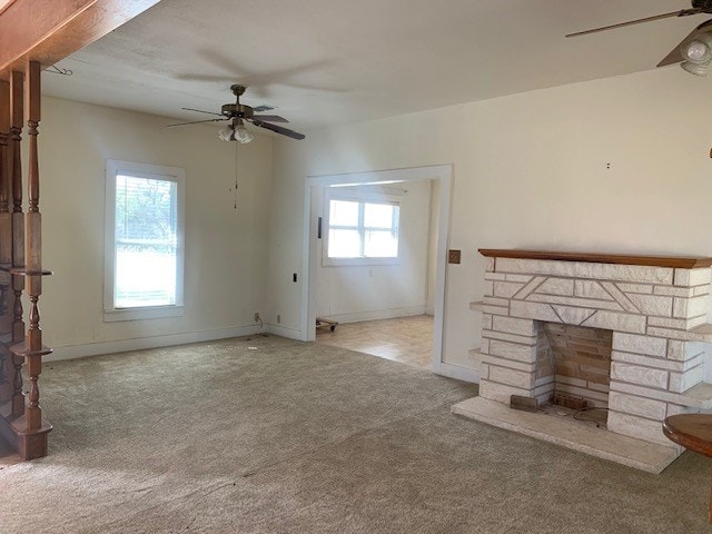 unfurnished living room with light colored carpet, a stone fireplace, and ceiling fan