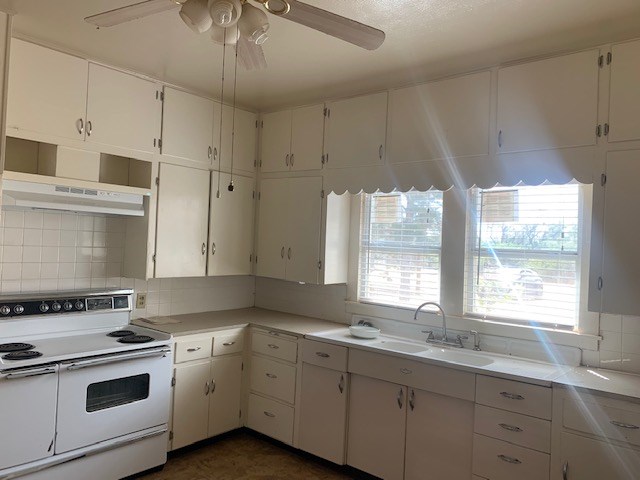 kitchen with tasteful backsplash, exhaust hood, sink, electric stove, and white cabinetry