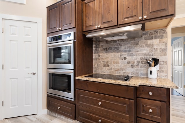 kitchen with tasteful backsplash, light stone counters, stainless steel double oven, black electric cooktop, and light hardwood / wood-style flooring