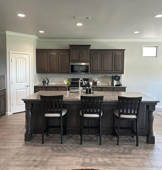 7103 Mcpherson Ln, Midland, TX 79706 - kitchen featuring stainless steel appliances, crown molding, a center island with sink, tasteful backsplash, and a kitchen bar