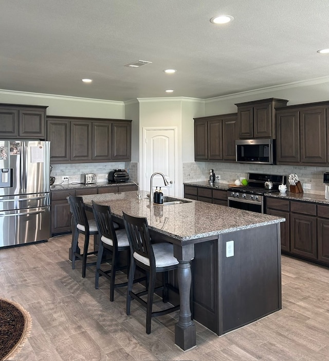 7103 Mcpherson Ln, Midland, TX 79706 - kitchen featuring stainless steel appliances, ornamental molding, decorative backsplash, a kitchen island with sink, and a kitchen breakfast bar
