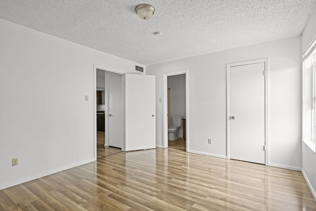 unfurnished bedroom with ensuite bathroom, light hardwood / wood-style floors, and a textured ceiling