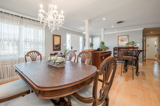 dining area with crown molding, decorative columns, light wood-type flooring, and an inviting chandelier