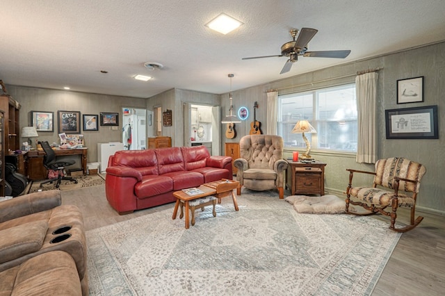 living room with ceiling fan, a textured ceiling, and light hardwood / wood-style flooring