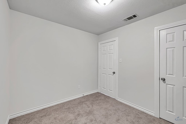 empty room with a textured ceiling and light colored carpet