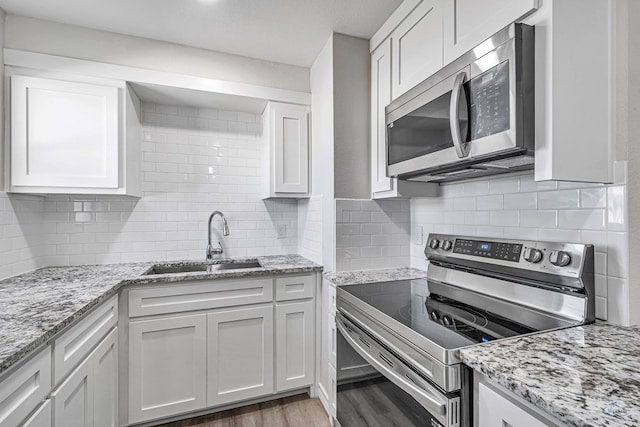 kitchen with sink, white cabinets, light wood-type flooring, and appliances with stainless steel finishes