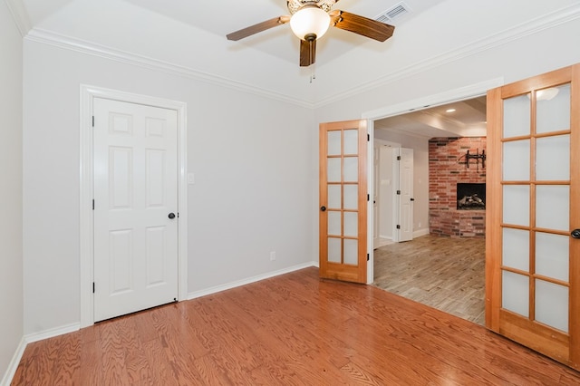 unfurnished room with a fireplace, crown molding, light hardwood / wood-style flooring, and french doors