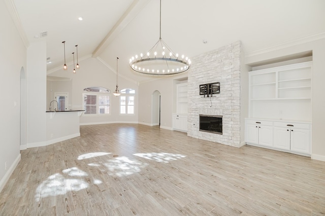 unfurnished living room featuring sink, light hardwood / wood-style flooring, a notable chandelier, a stone fireplace, and beamed ceiling