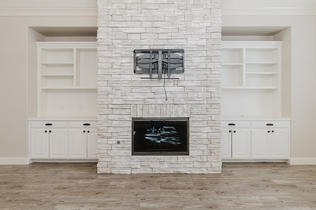 unfurnished living room with ornamental molding, a stone fireplace, and light hardwood / wood-style flooring