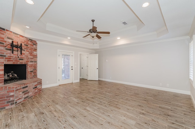 unfurnished living room featuring a fireplace, ornamental molding, ceiling fan, a raised ceiling, and light wood-type flooring