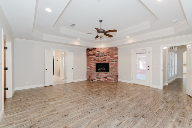 unfurnished living room with a raised ceiling, ceiling fan, a brick fireplace, and light hardwood / wood-style floors