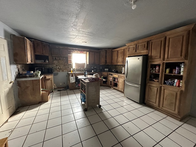 kitchen with a textured ceiling, light tile patterned flooring, a center island, and stainless steel refrigerator