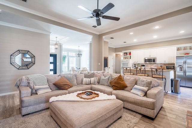 living room with light wood-style flooring, recessed lighting, ceiling fan with notable chandelier, baseboards, and ornamental molding