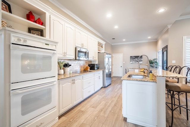 kitchen featuring open shelves, appliances with stainless steel finishes, a sink, and a breakfast bar