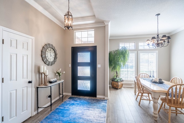 foyer entrance featuring baseboards, ornamental molding, wood finished floors, a textured ceiling, and a chandelier