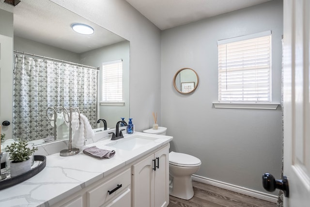 bathroom with a wealth of natural light, baseboards, toilet, and wood finished floors