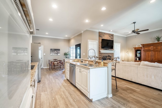 kitchen featuring a brick fireplace, open floor plan, a sink, light wood-type flooring, and a kitchen bar