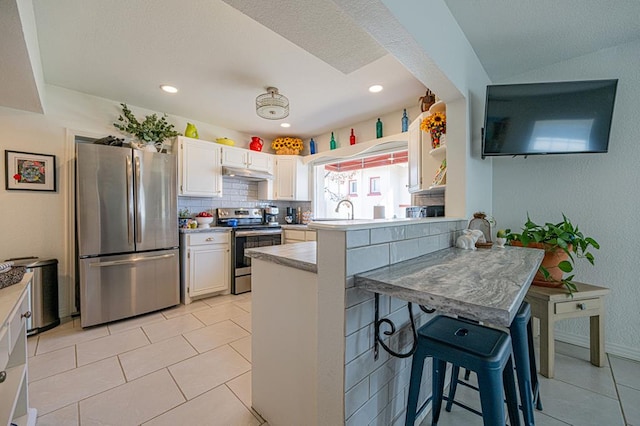 kitchen with stainless steel appliances, kitchen peninsula, a kitchen bar, decorative backsplash, and white cabinets