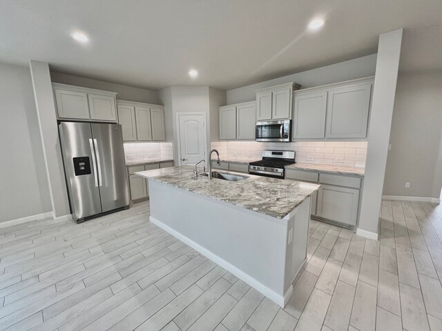 3108 Mearns Ct, Midland, TX 79705 - kitchen featuring stainless steel appliances, a sink, light wood-style flooring, decorative backsplash, and an island with sink