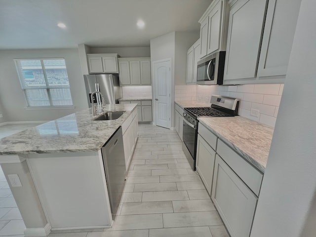 3108 Mearns Ct, Midland, TX 79705 - kitchen featuring stainless steel appliances, a sink, tasteful backsplash, a center island with sink, and light stone counters