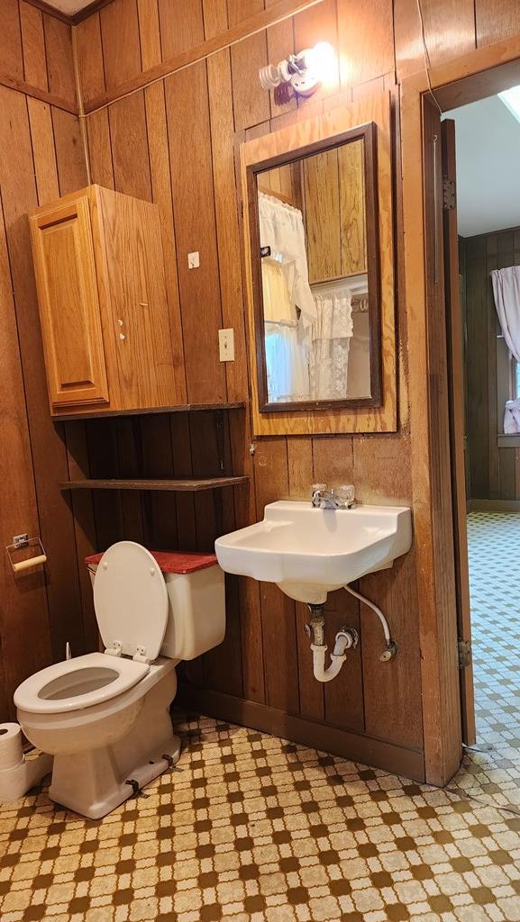 bathroom featuring toilet, wooden walls, a sink, and tile patterned floors