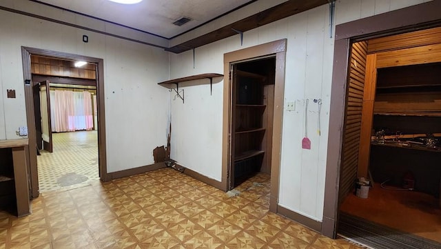 corridor with visible vents, wood walls, and light floors