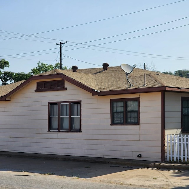 view of property exterior with roof with shingles and fence