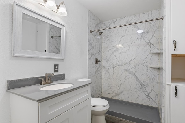 bathroom featuring vanity, toilet, wood-type flooring, and tiled shower