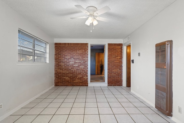 tiled empty room with ceiling fan, brick wall, and a textured ceiling