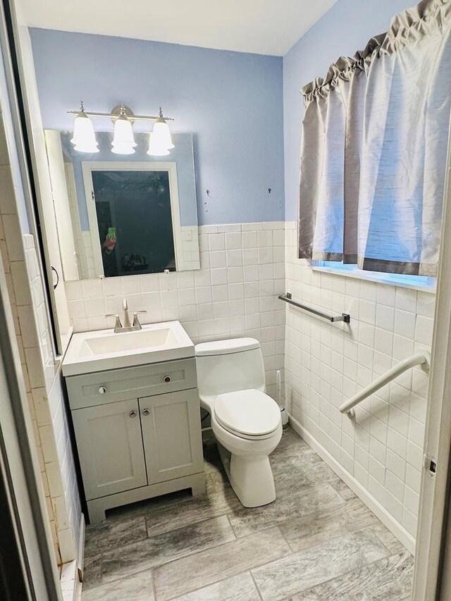 bathroom featuring wood-type flooring, vanity, toilet, and tile walls