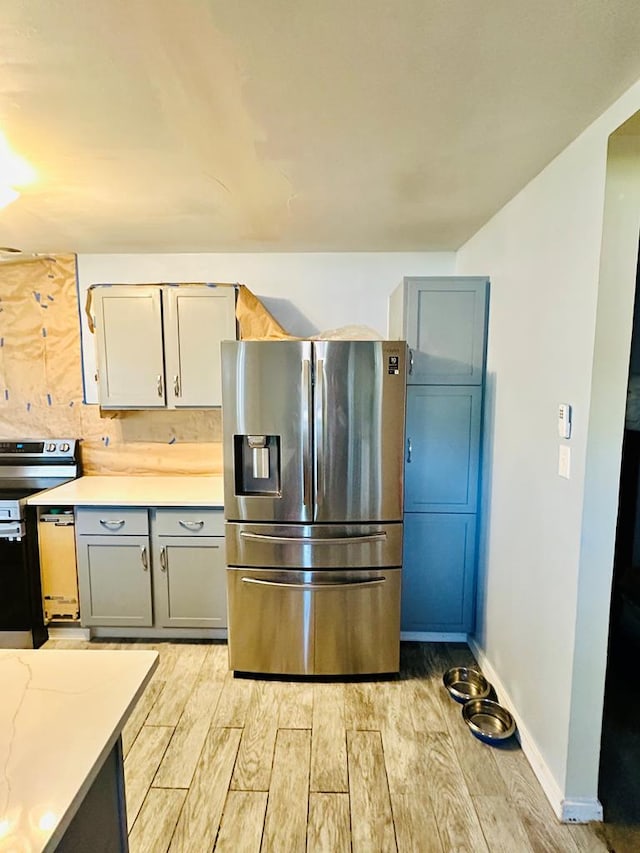 kitchen with decorative backsplash, stainless steel refrigerator with ice dispenser, light wood-type flooring, range, and gray cabinets