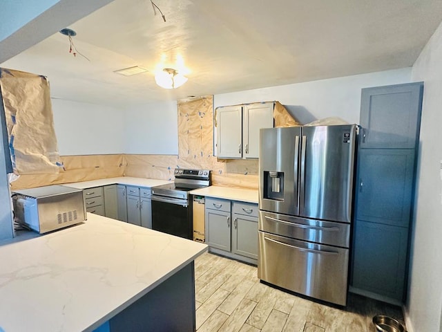 kitchen featuring gray cabinetry, light hardwood / wood-style floors, light stone countertops, and appliances with stainless steel finishes