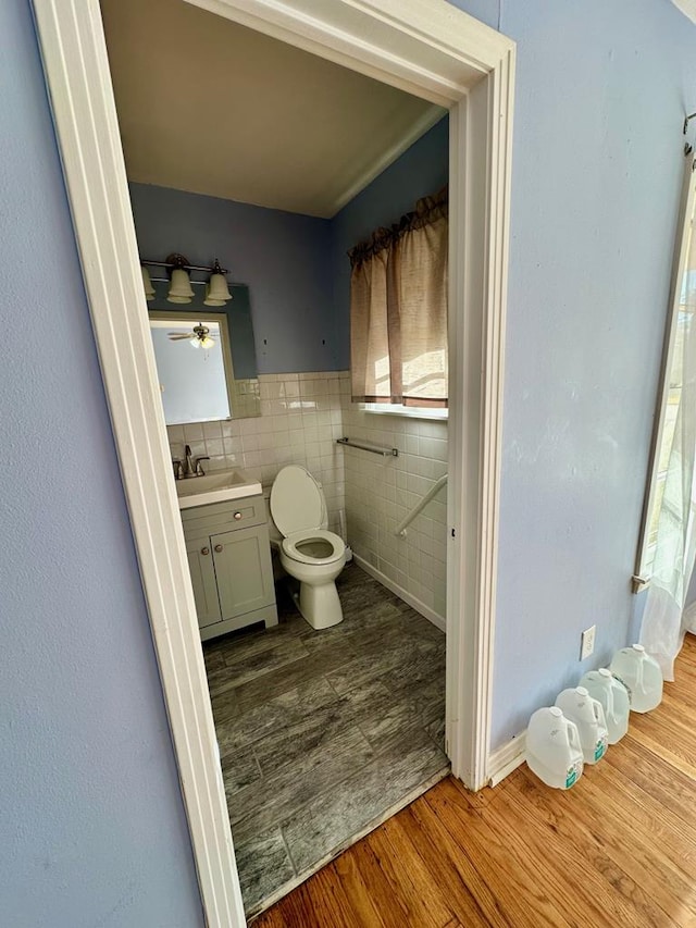 bathroom with a healthy amount of sunlight, toilet, wood-type flooring, and tile walls