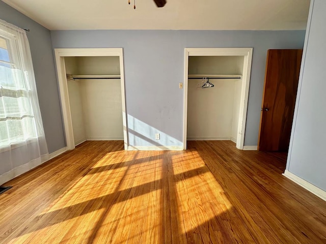 unfurnished bedroom featuring light wood-type flooring, multiple windows, and multiple closets